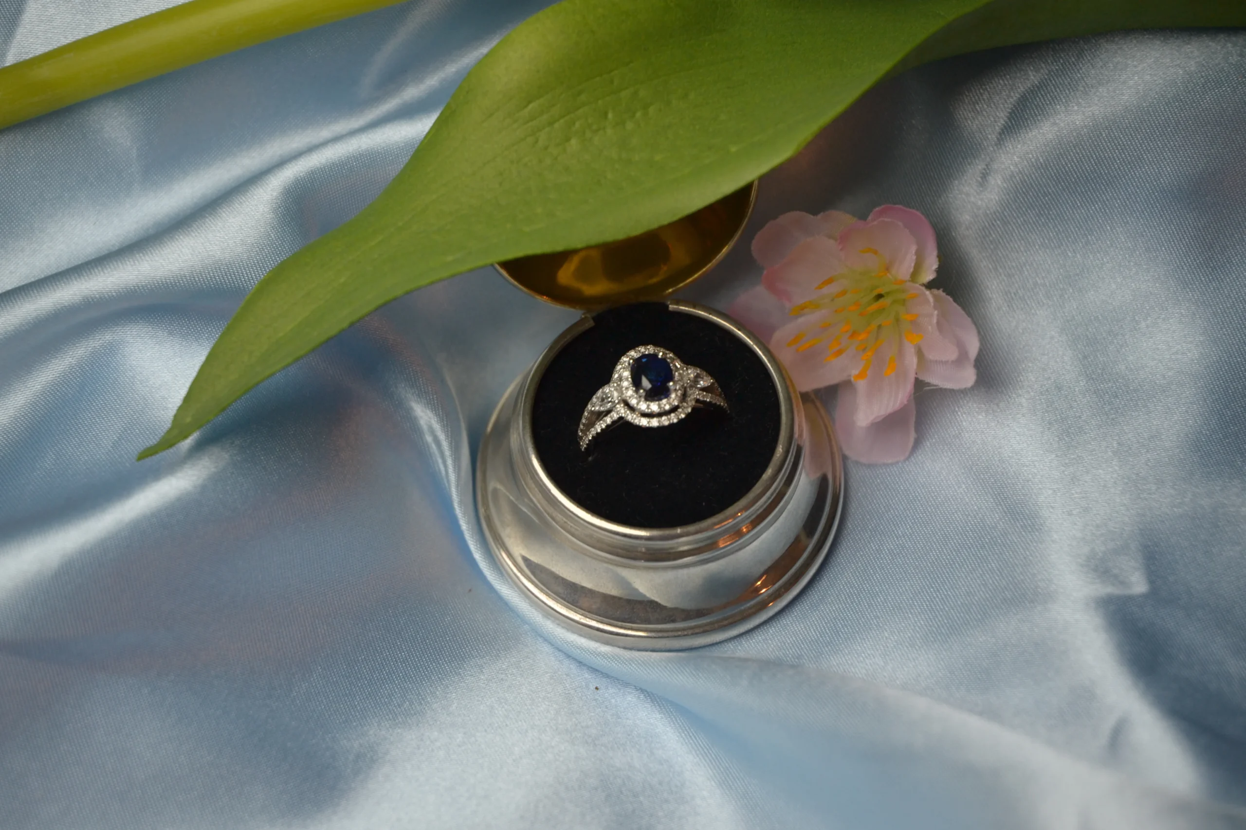 Handcrafted bespoke sapphire and diamond halo engagement ring in a round silver presentation box by Alexander Jewellery in Chichester.