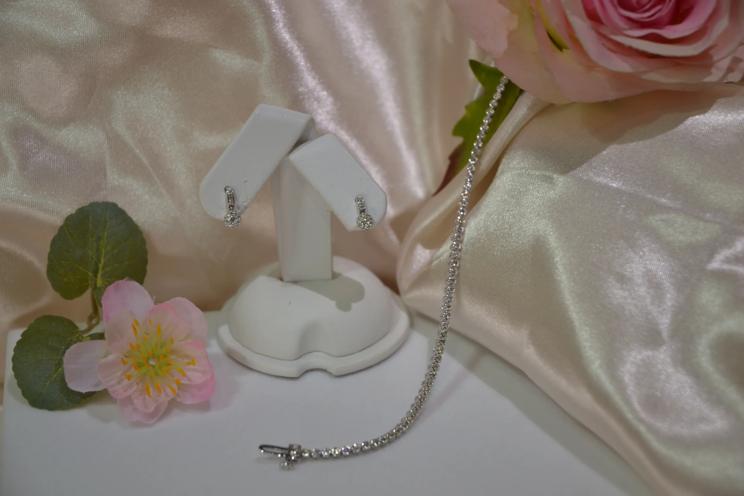 Elegant bespoke diamond drop earrings on a display stand alongside a diamond tennis bracelet on cream silk at Alexander Jewellery Chichester.