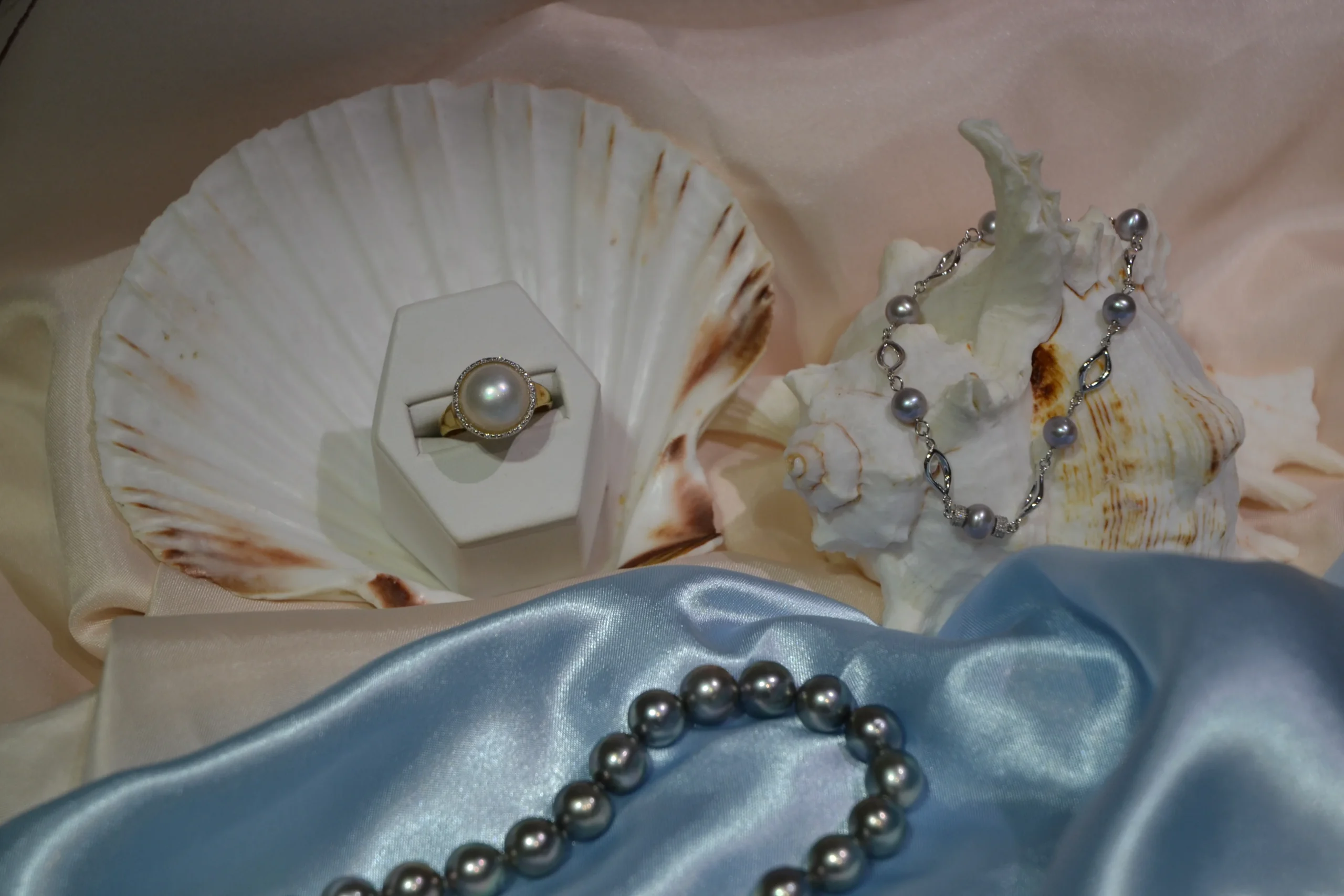 Bespoke pearl jewellery collection including a large pearl ring in a shell, delicate pearl bracelet, and dark pearl necklace by Alexander Jewellery Chichester.