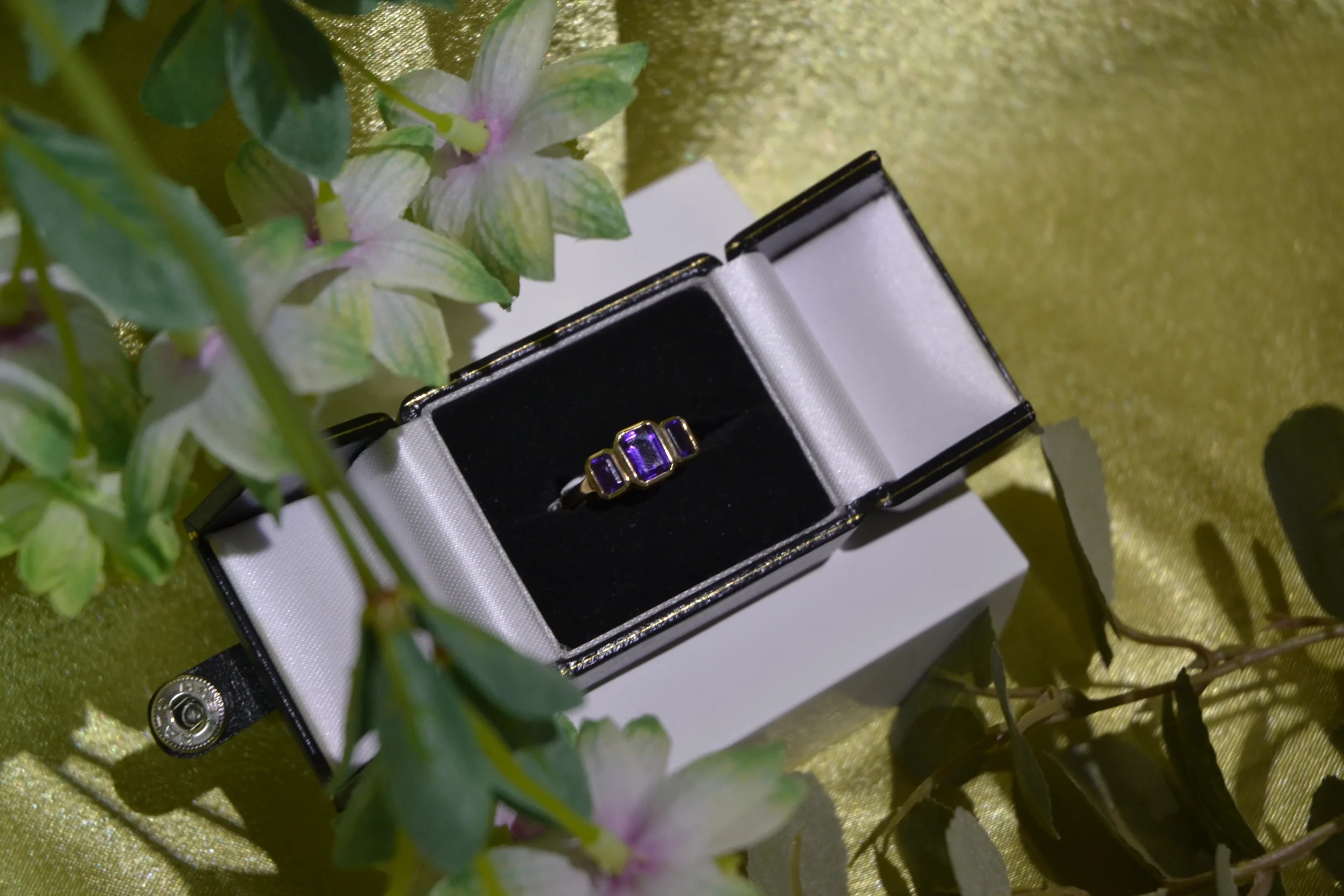 Custom remodelled three-stone purple gemstone gold ring in a gift box, designed by expert jewellers at Alexander Jewellery Chichester.
