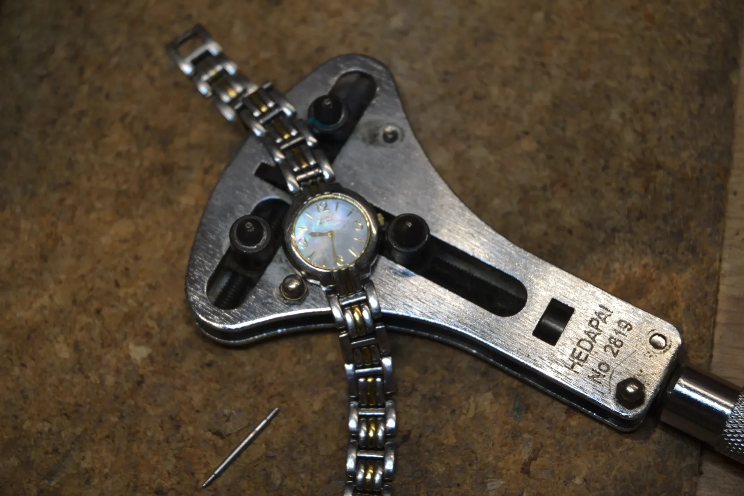Ladies two-tone watch secured in a professional metal case opener tool for expert watch repairs and servicing at Alexander Jewellery in Chichester.
